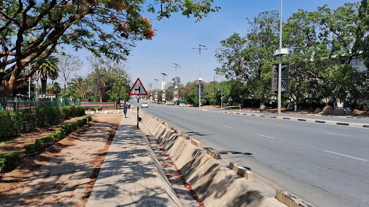 A clean, wide pavement along Independence Avenue in Lusaka, with young trees, a planted verge and the road beside it